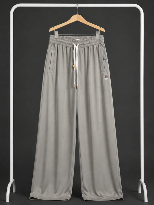 Light gray wide-leg sweatpants with an elastic waistband, white drawstring, and side pockets, hanging on a wooden hanger from a white clothing rack against a dark gray background.