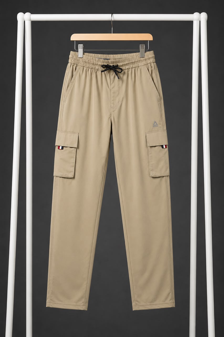 Beige cargo pants with a black drawstring waist, hanging on a wooden hanger from a white clothing rack against a dark gray background.