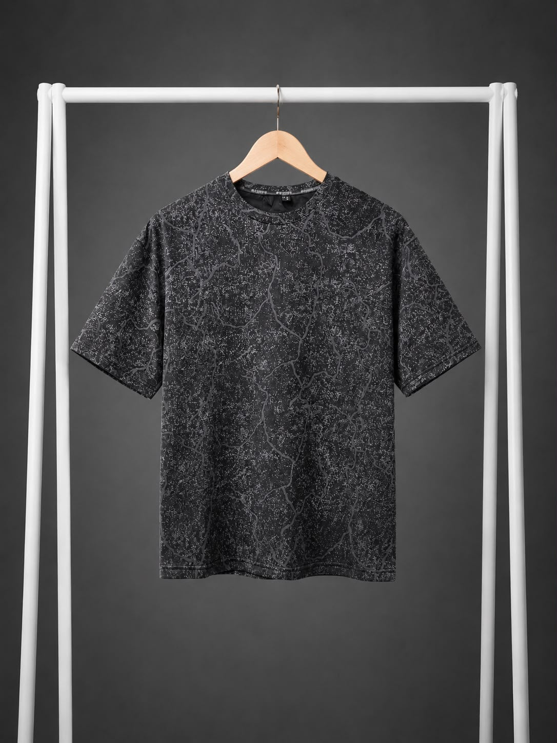A short-sleeve crewneck t-shirt with a dark gray and black marbled pattern, hanging on a wooden hanger from a white clothing rack against a dark gray background.