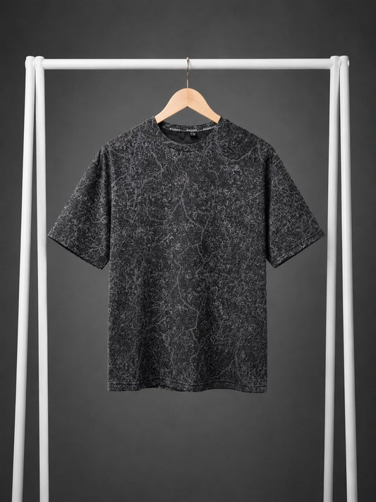 A short-sleeve crewneck t-shirt with a dark gray and black marbled pattern, hanging on a wooden hanger from a white clothing rack against a dark gray background.